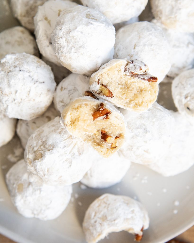 Two open halves of a pecan snowball cookie showing the shortbread middle, and pecans inside.