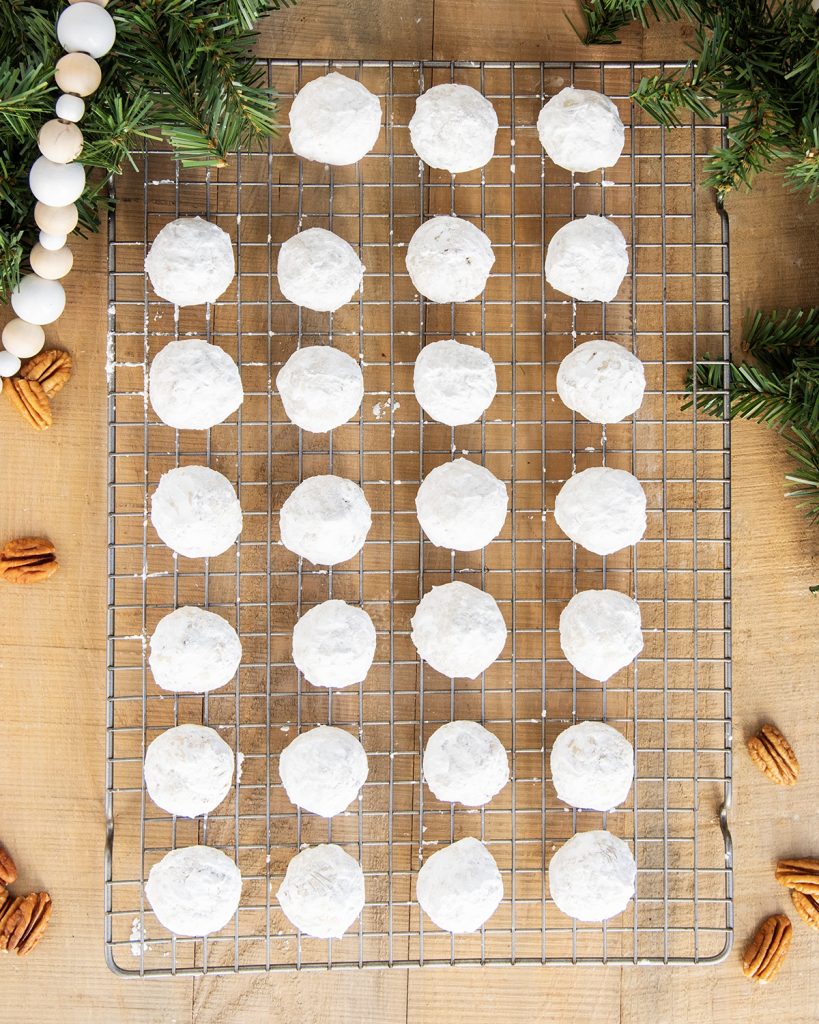 Rows of Pecan snowball cookies covered in powdered sugar on a wire cooling rack.
