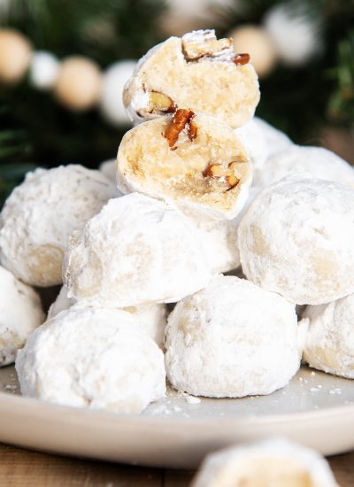A stack of pecan snowball cookies on a plate, with two halves of a cookie stacked on top showing the middle.