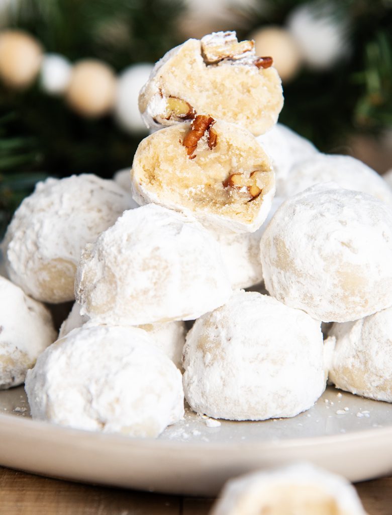 A stack of pecan snowball cookies on a plate, with two halves of a cookie stacked on top showing the middle.