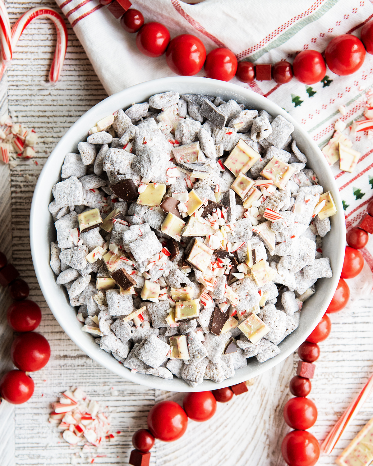 An overhead photo of a bowl of Chocolate Muddy Buddies topped with peppermint bark pieces and candy cane pieces.