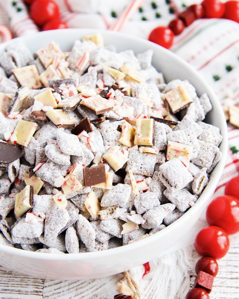 A bowl of Puppy Chow with white chocolate peppermint bark candy pieces in it.