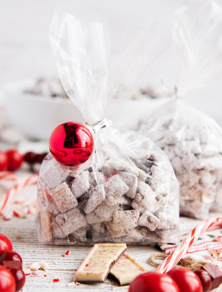 A cellophane bag of Peppermint Bark Muddy Buddies with a small red ornament tied to the bag.