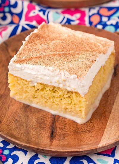 A piece of tres leches cake on a wooden plate.