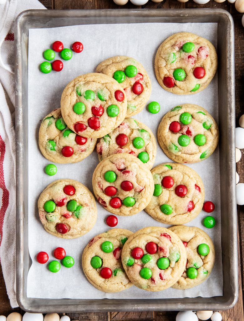 An overhead photo of a baking pan topped with Christmas M&M cookies, and red and green M&Ms.