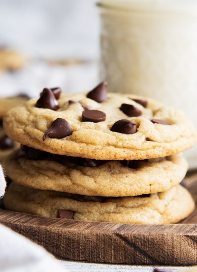 A stack of three chocolate chip cookies on a wooden tray.