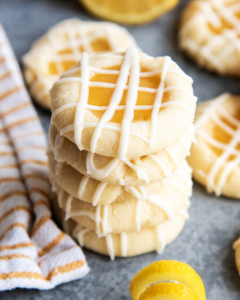 A stack of lemon curd thumbprint cookies with drizzles of a hardened vanilla icing over the top.