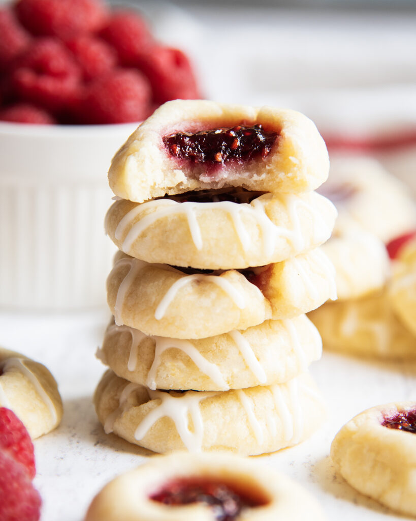 A stack of Raspberry Almond Thumbprint Cookies, and the top cookie has a bite out of it.
