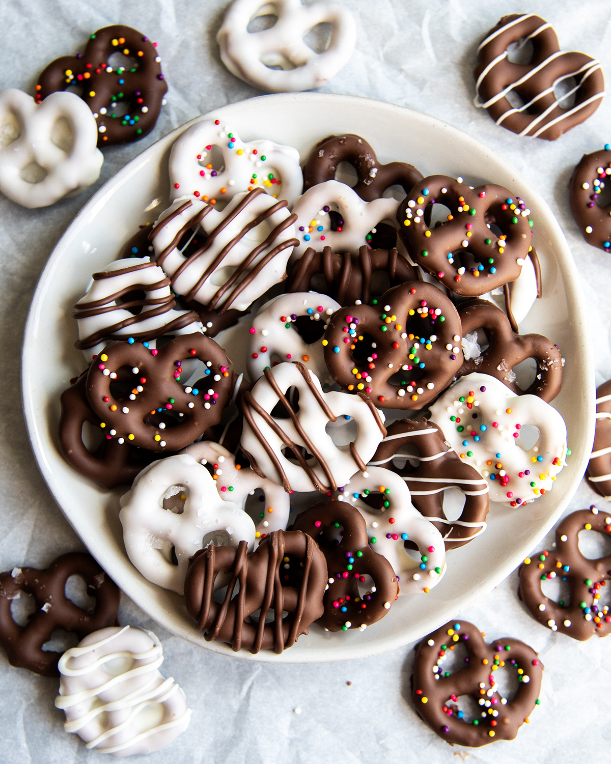 An above photo of chocolate covered pretzels on a plate, some are white chocolate and some are milk chocolate.