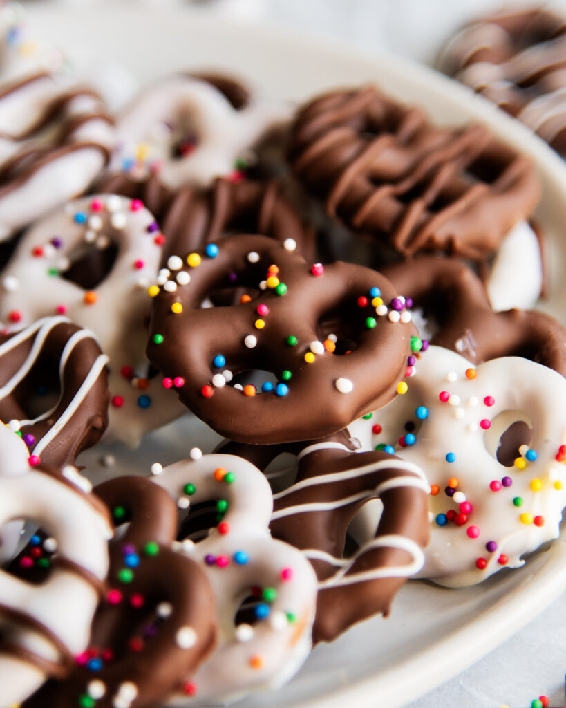 A plate of chocolate covered pretzels topped with non pareil sprinkles.