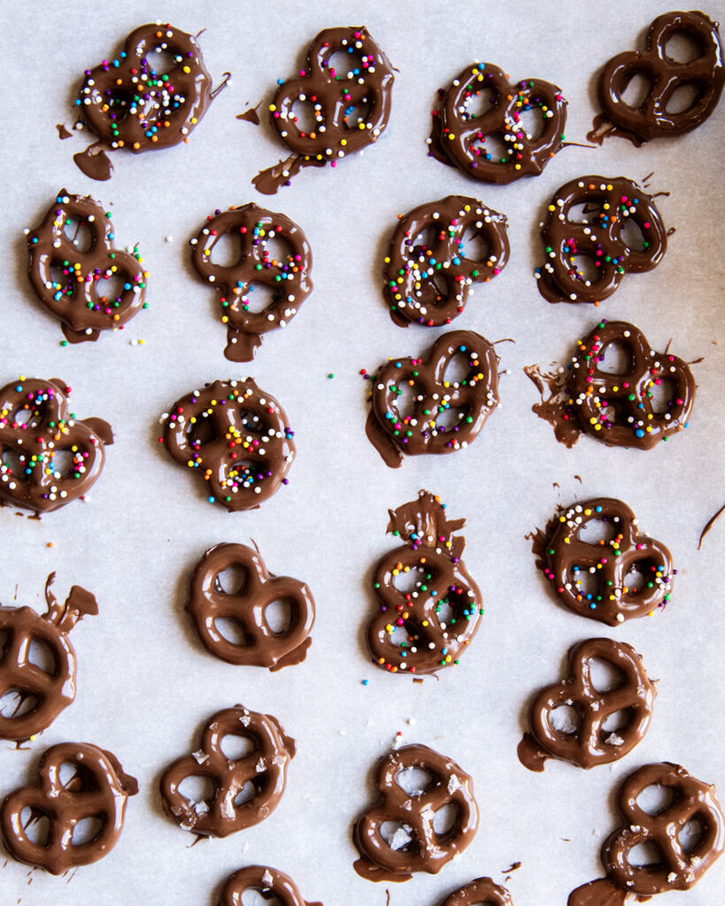 Pretzels topped with melted chocolate and small round sprinkles.