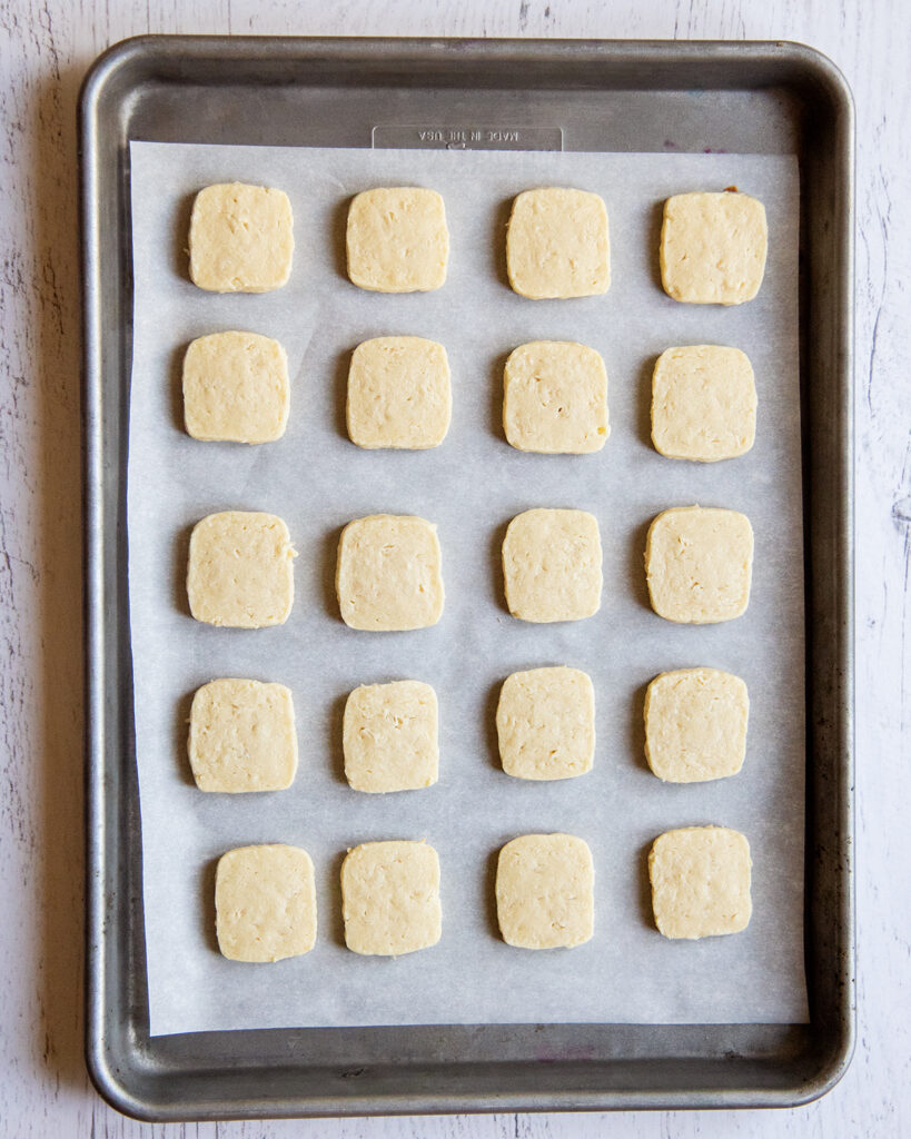 An above photo of a a cookie sheet topped with square coconut shortbread cookies.