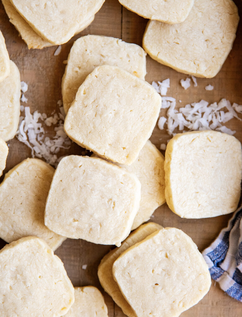 An above photo of square shortbread cookies, with coconut flakes next to them.