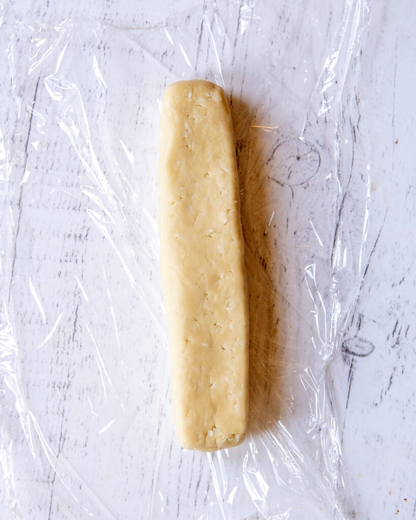 An above photo of a log of coconut shortbread cookie dough on a piece of plastic wrap.