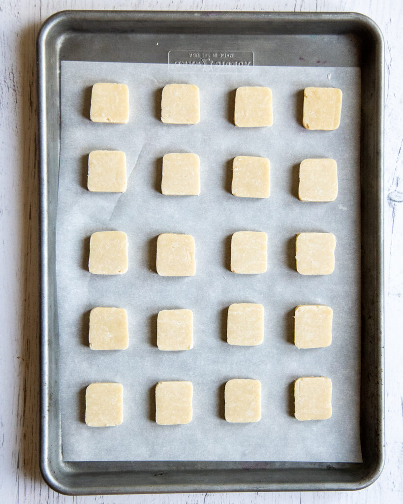 Square uncooked shortbread cookies on a baking tray.