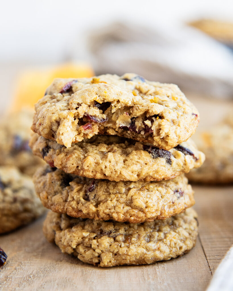 A stack of 4 cranberry oatmeal cookies on a wooden table, the top cookie has a bite out of it.
