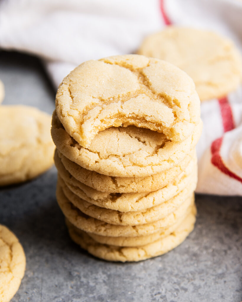 A stack of chewy sugar cookies, and the top cookie has a bite out of it.