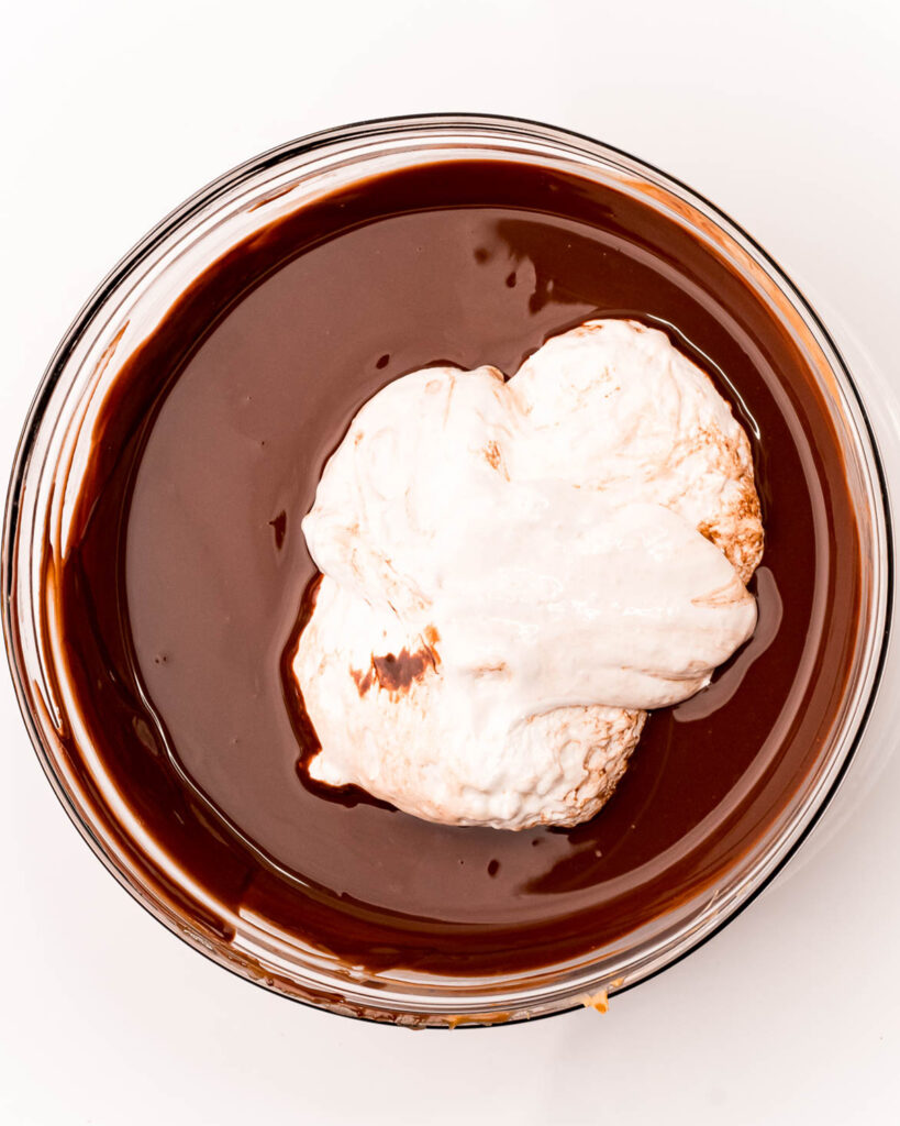 A bowl of melted chocolate with a big portion of marshmallow fluff in the middle.