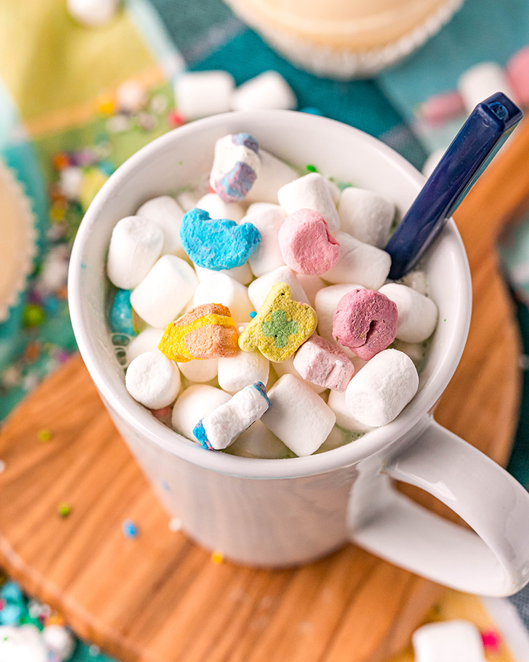 A white mug full of hot cocoa and topped with mini marshmallows and lucky charms marshmallows.