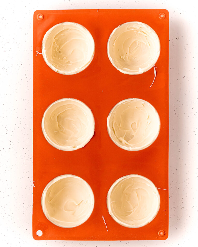An overhead photo of a red silicone mold full of domes of white chocolate.