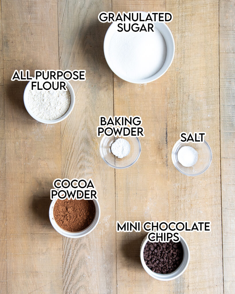 The 6 ingredients needed to make homemade brownie mix in small bowls on a table.