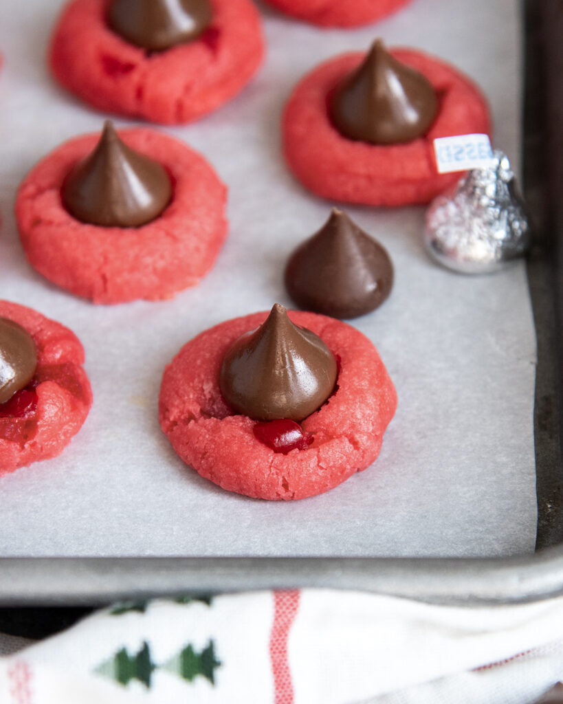 Red blossom cookies topped with a Hershey Kiss on a cookie sheet.