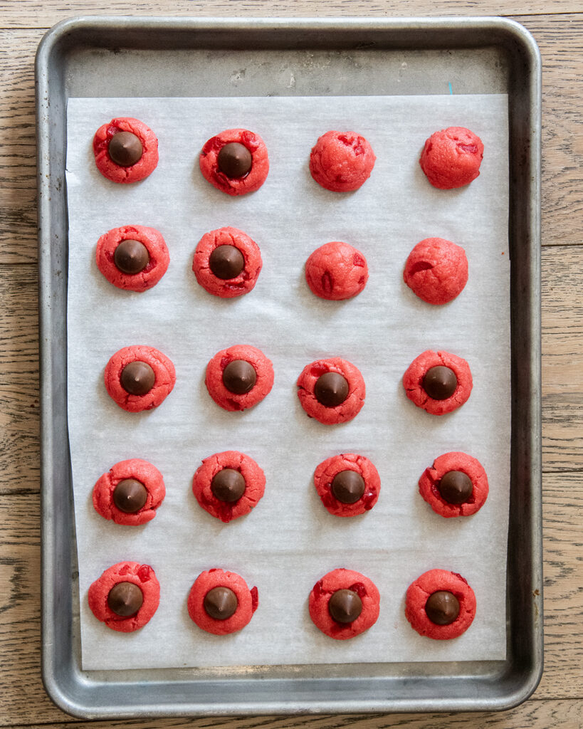 Baked Cherry Kiss cookies on a cookie sheet lined with parchment paper.