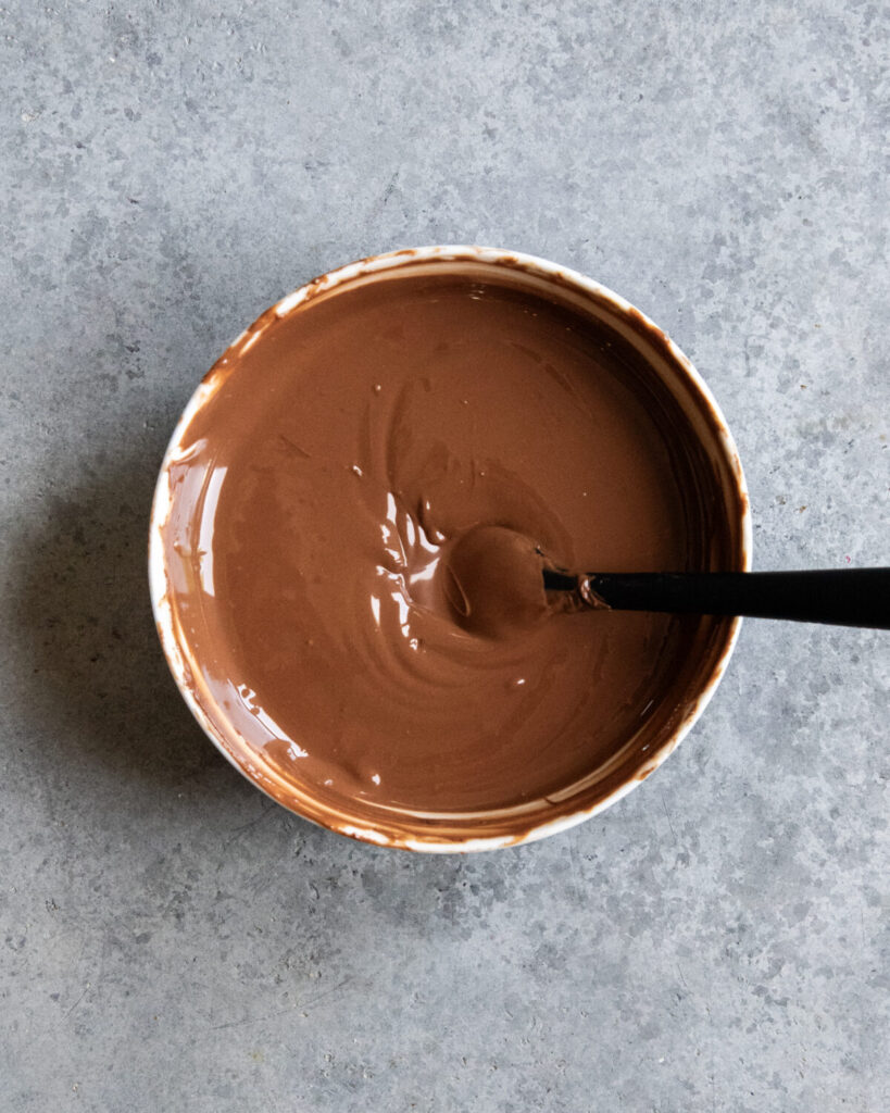 A bowl of melted chocolate with a rubber spatula in it.