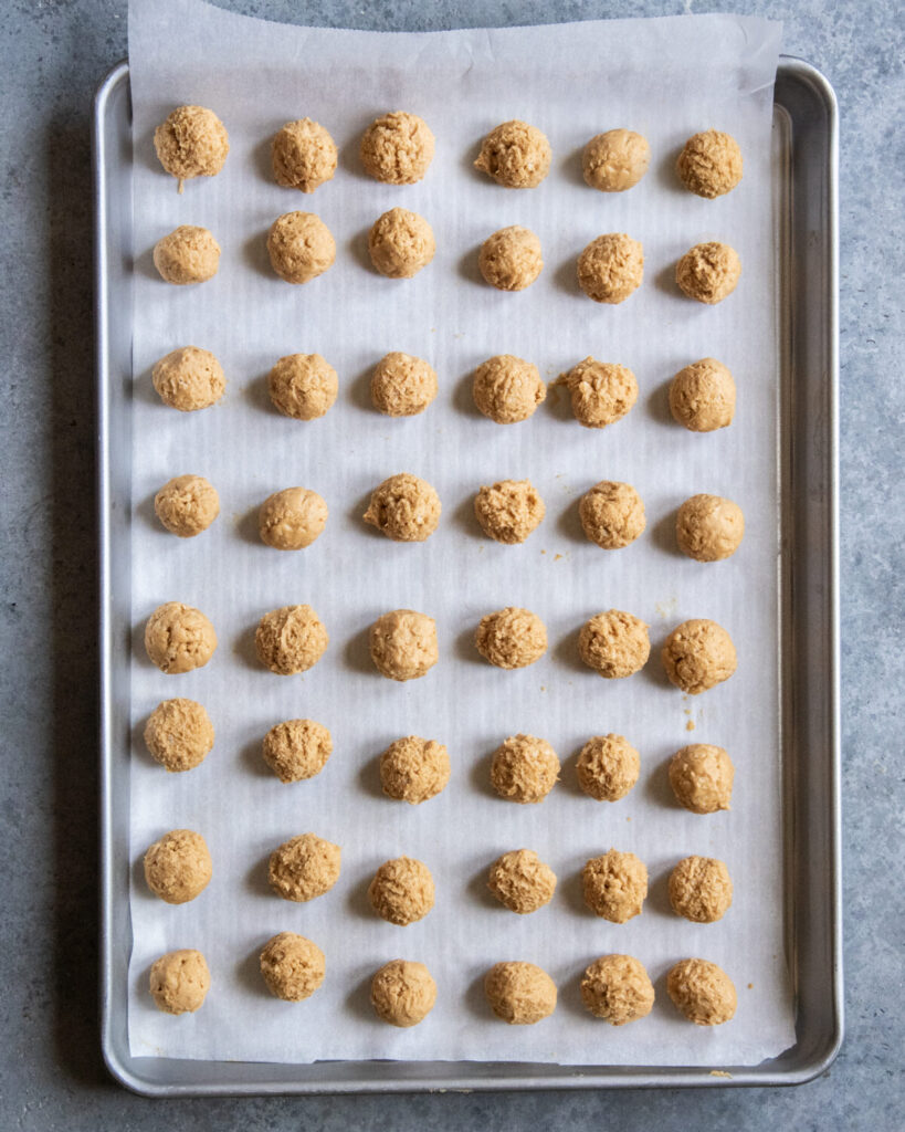 Rows o peanut butter and powdered sugar balls on a cookie sheet.