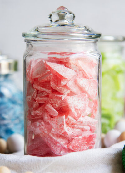 A tall glass jar full of sharp red pieces of candy coated with powdered sugar.