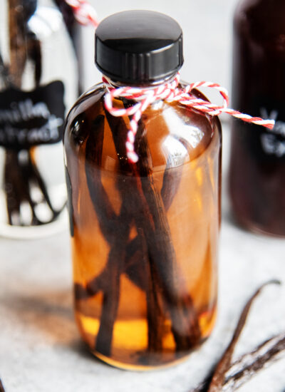 A glass bottle with an amber colored liquid, and vanilla beans in it.