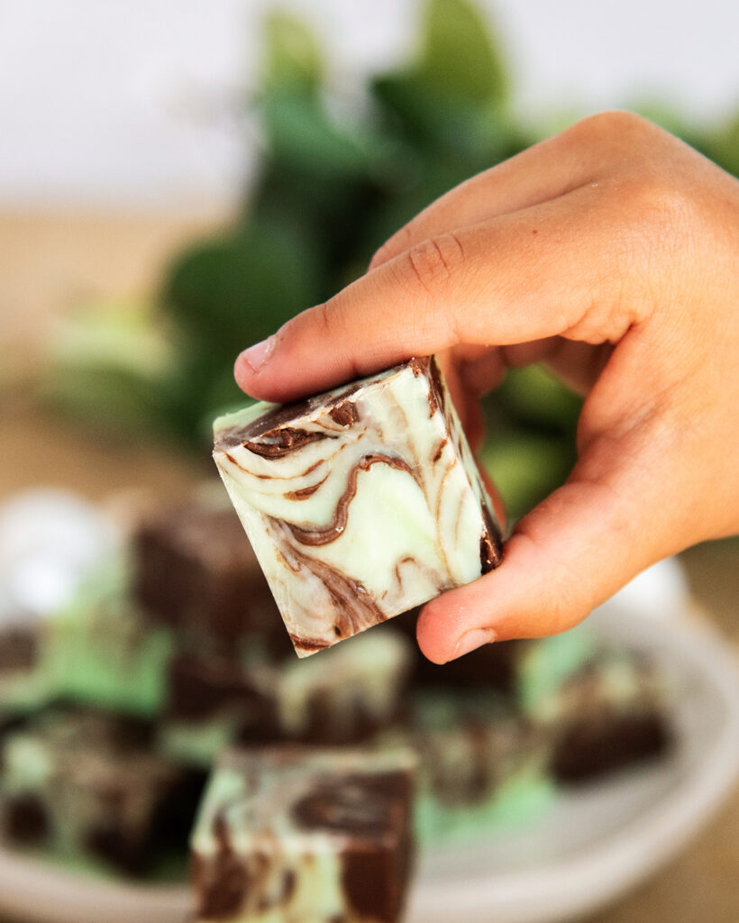 A child's hand holding a piece of green mint and chocolate swirled fudge.