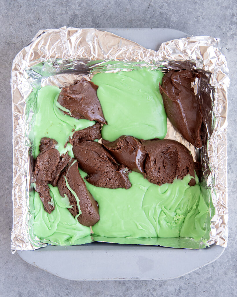 Dollops of green mint fudge and chocolate fudge in a square pan.