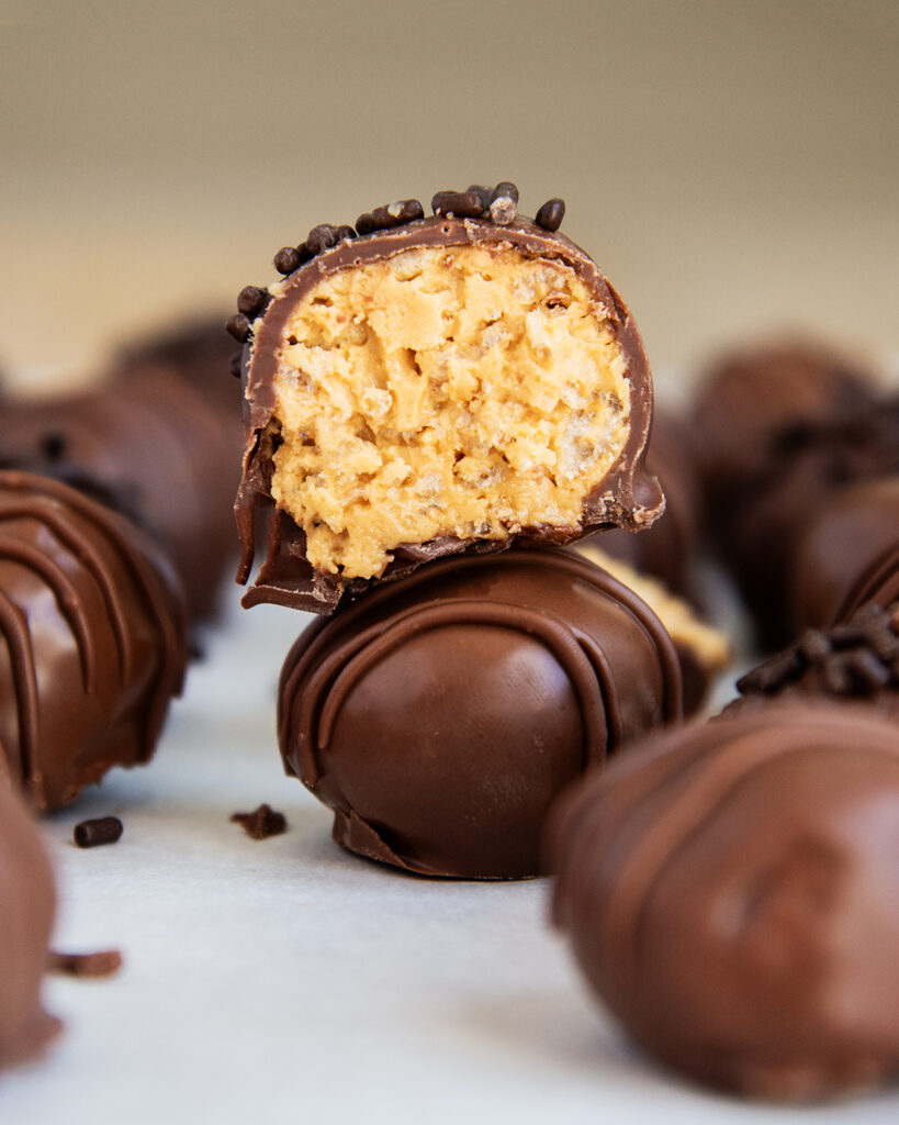 Two peanut butter rice crispy balls stacked, the top one is cut in half showing the peanut butter mixture in the middle.