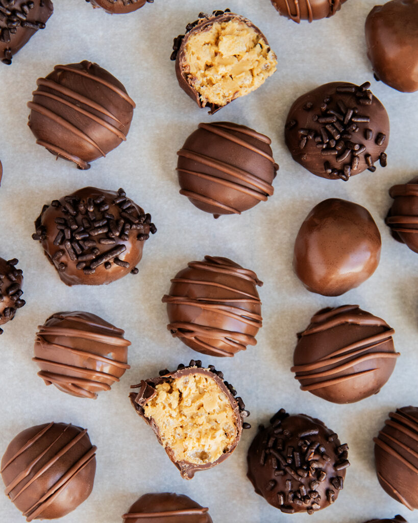 An overhead photo of chocolate peanut butter truffles on a piece of parchment paper, two are cut in half showing the peanut butter mixture in the middle.