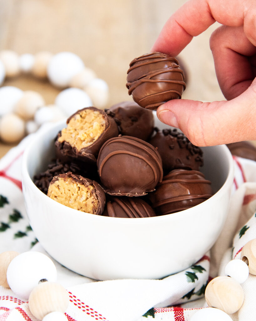 A hand grabbing a peanut butter truffle off a pile of them in a bowl.