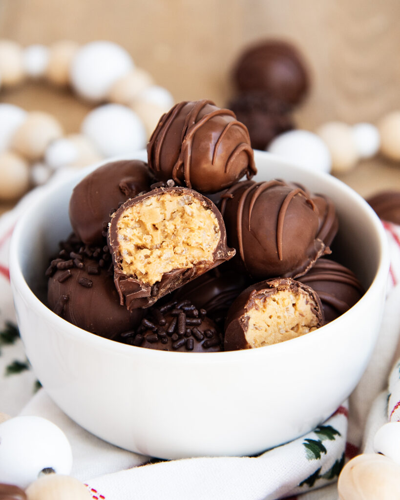 A bowl of crispy peanut butter balls dipped in chocolate. Some are cut in half showing the peanut butter centers.