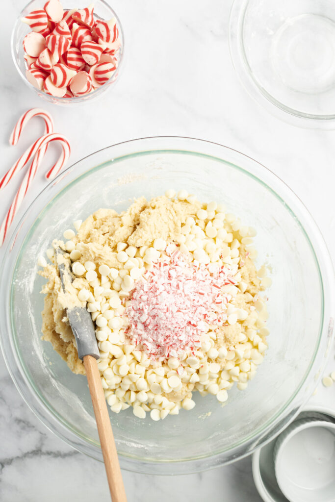 An above view of a glass bowl with cookie dough topped with candy cane pieces, and white chocolate chips.