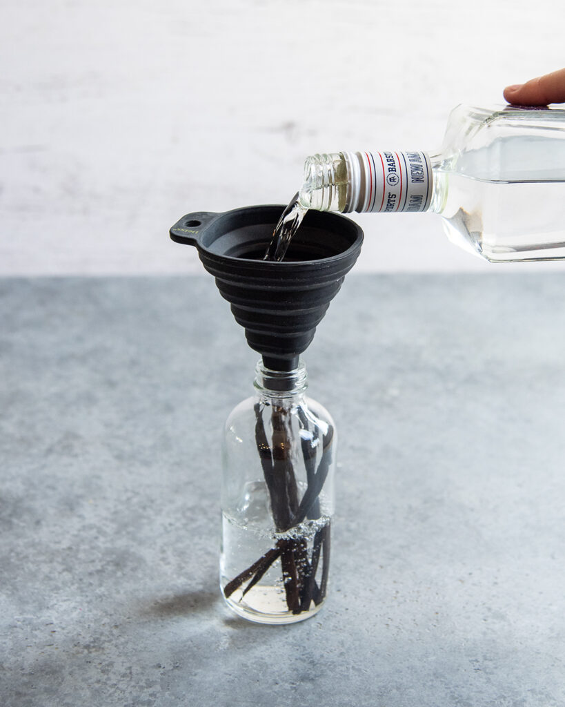 Vodka being poured in a glass bottle through a black funnel.