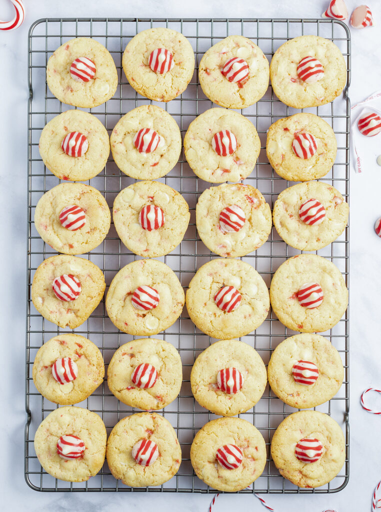 A cooling rack topped with round sugar cookies, each topped with a red and white striped Hershey kiss.