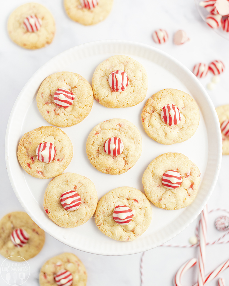 An above view of a plate of round cookies each topped with a red and white Candy Cane Hershey's Kiss.