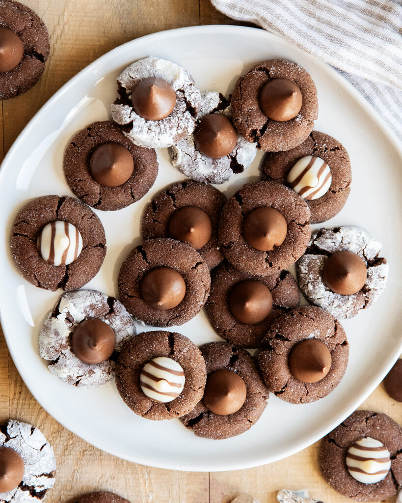 An above view of a plate of chocolate blossom cookies topped with Hershey's Kisses and Hugs.