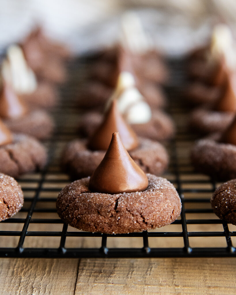 Rows of Chocolate Thumbprint Cookies topped with Hershey Kiss candies on a wire rack.