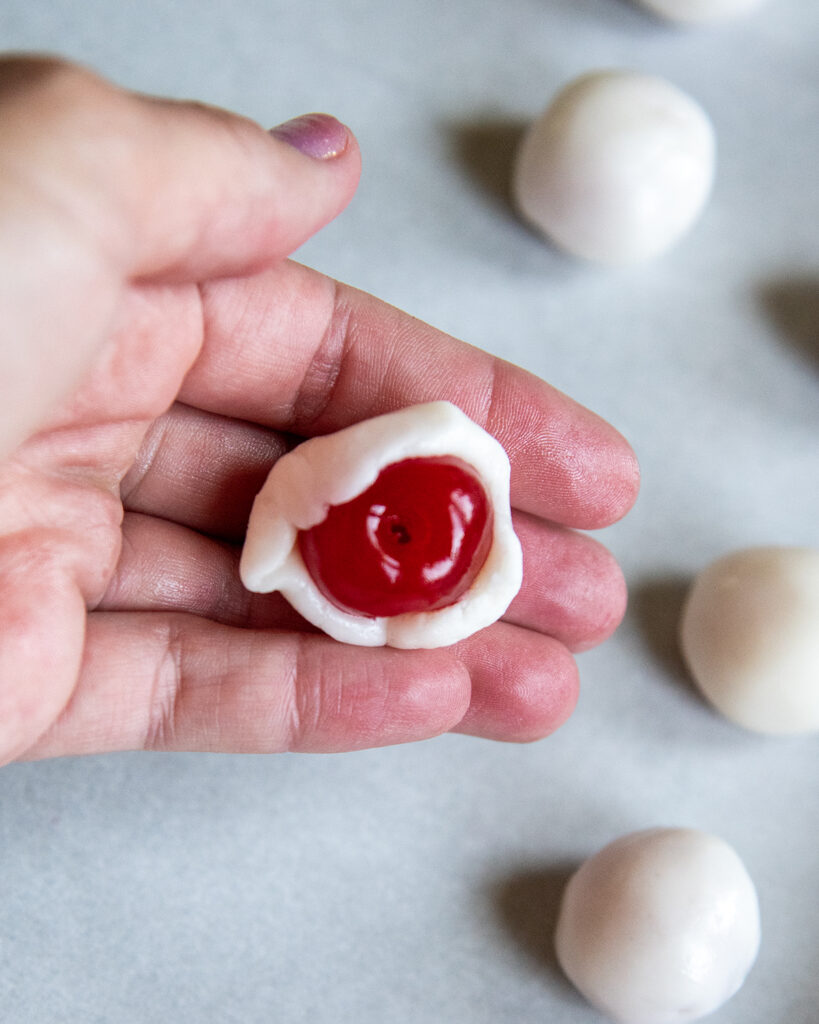 A hand holding a cherry partially covered in powdered sugar fondant. 