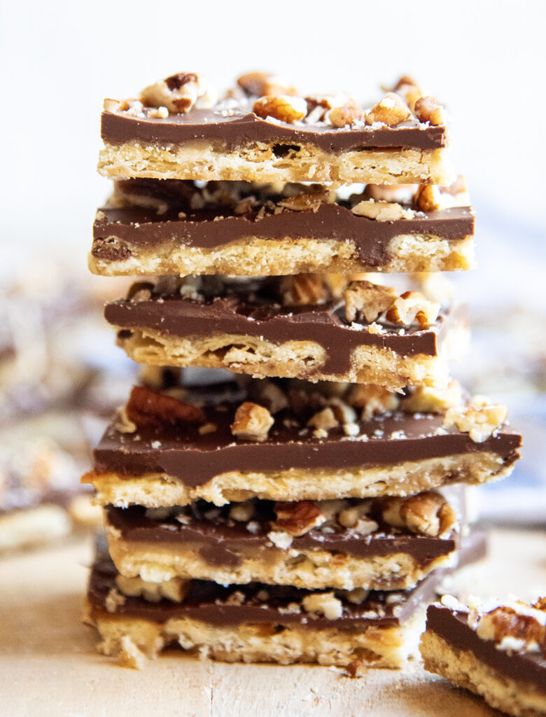 A stack of pieces of cracker toffee topped with chocolate and pecans.