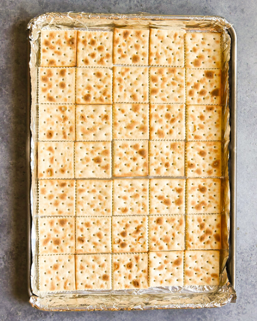 A cookie sheet lined with foil, and with rows of saltine cookies.