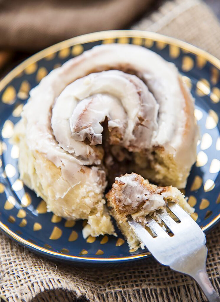 A cinnamon roll on a plate with a bite cut off and on a fork.