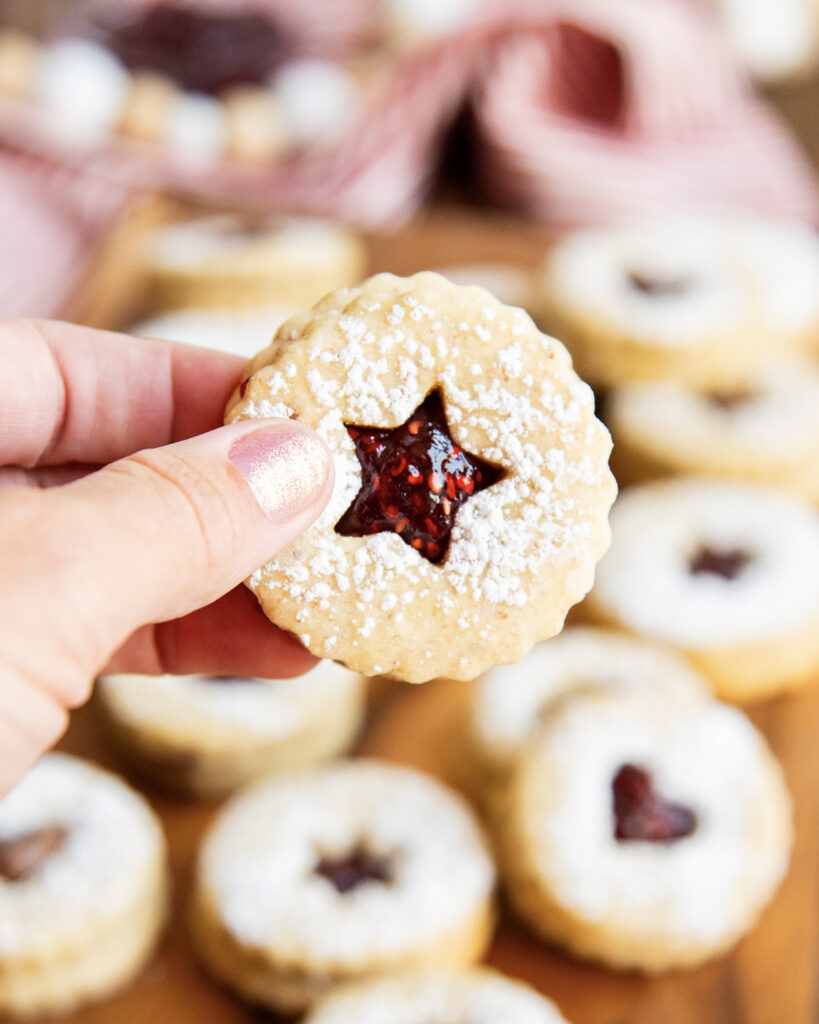 A hand holding a linzer cookie with a star cut out full of jam.