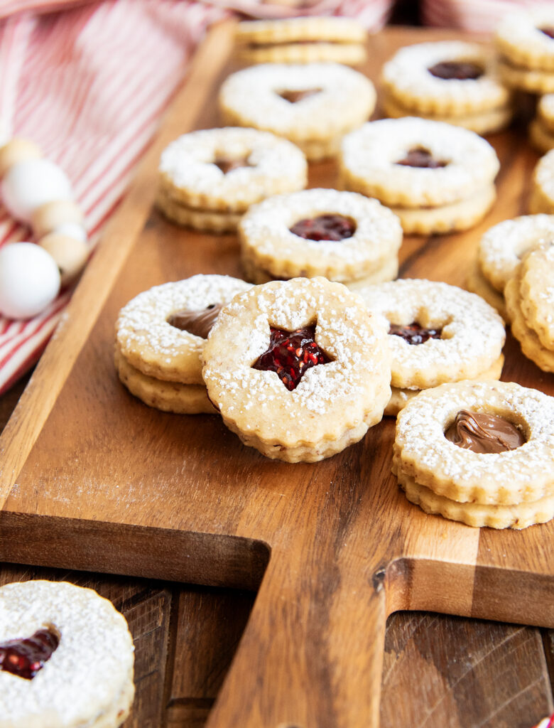 A pile of Linzer tart cookies on a wooden cutting board.