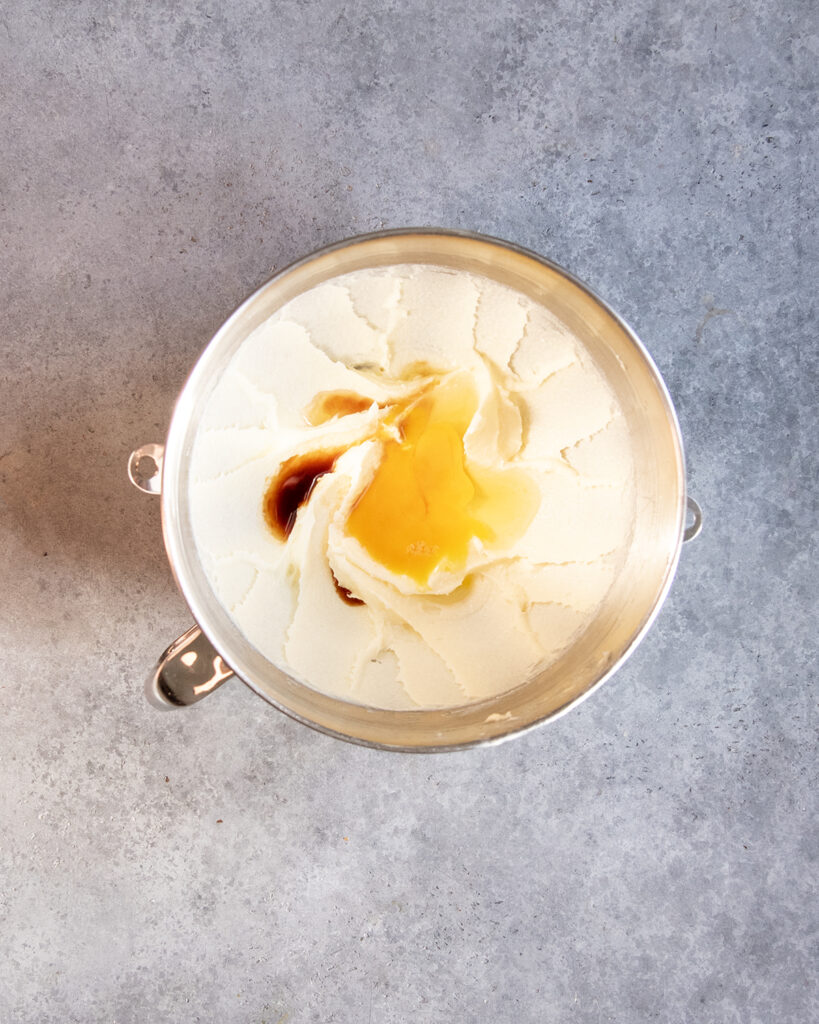 A bowl of creamed butter and sugar topped with a raw egg, and vanilla extract. 